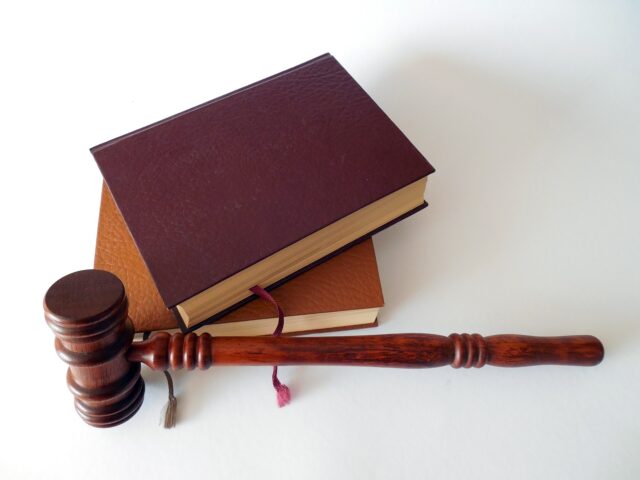 A wooden judge's gavel rests beside two stacked, leather-bound books on a light background.