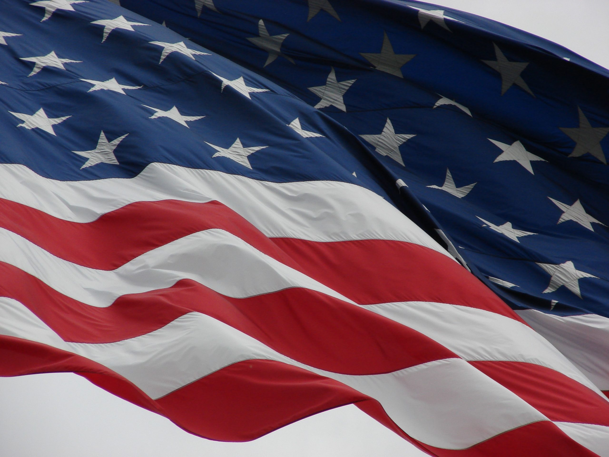 Close-up of the American flag waving against a gray sky, reminiscent of resilience in times of struggle. The image captures the stars on the blue field and red and white stripes, symbolizing unity through challenges such as military divorce.
