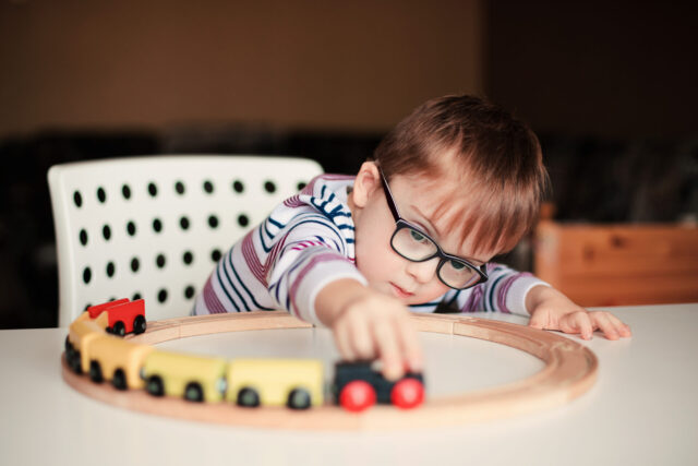 little boy with syndrome dawn playing with wooden train