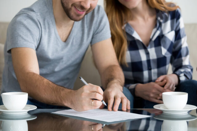 Close up view of couple signing documents, customers renters tenants or clients write signature on rental sale prenuptial agreement or rental contract paper buying real estate or services concept