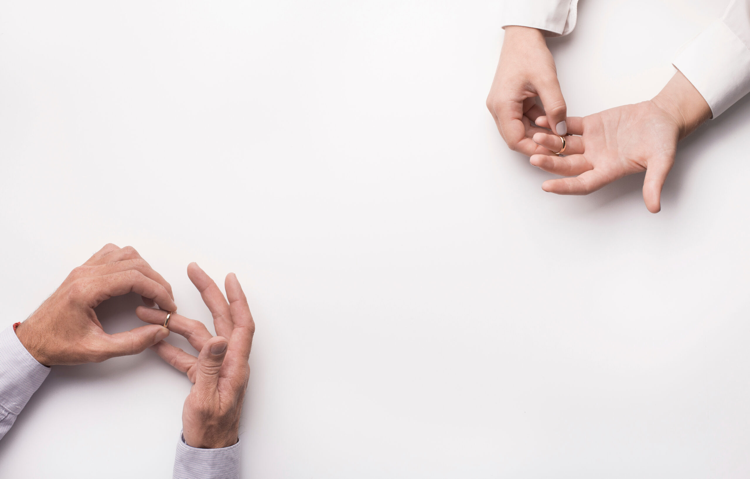 Two hands on the left, belonging to a person wearing a long-sleeved shirt, are seen removing a ring. On the right, another person's hands, also in a long-sleeved shirt, hold a ring. The background is plain white, with ample empty space in between.