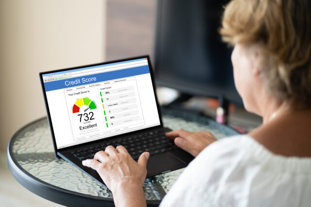 A person is using a laptop at a glass table, viewing a website displaying a credit score of 732, labeled as 