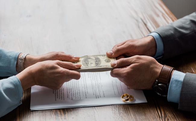 partial view of lawyer and client holding dollar banknotes above divorce decree with wedding rings 