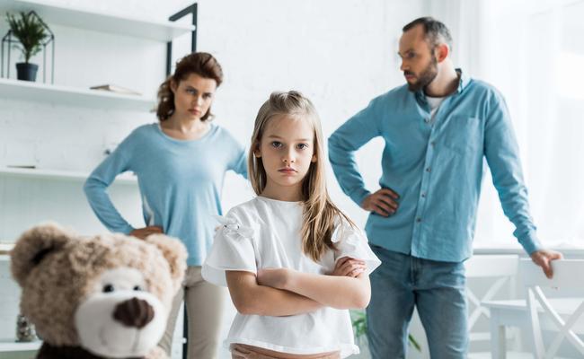 selective focus of cute kid standing with crossed arms near teddy bear and parents at home