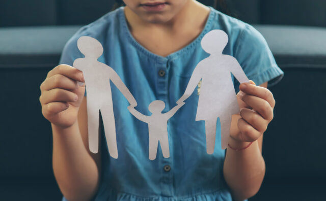 Child with a paper family in his hands. the concept of divorce, custody and child abuse. Selective focus.